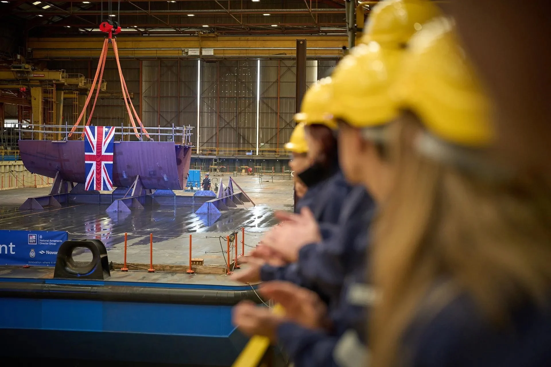 A large ship under construction in a shipyard, with a focus on the keel section.