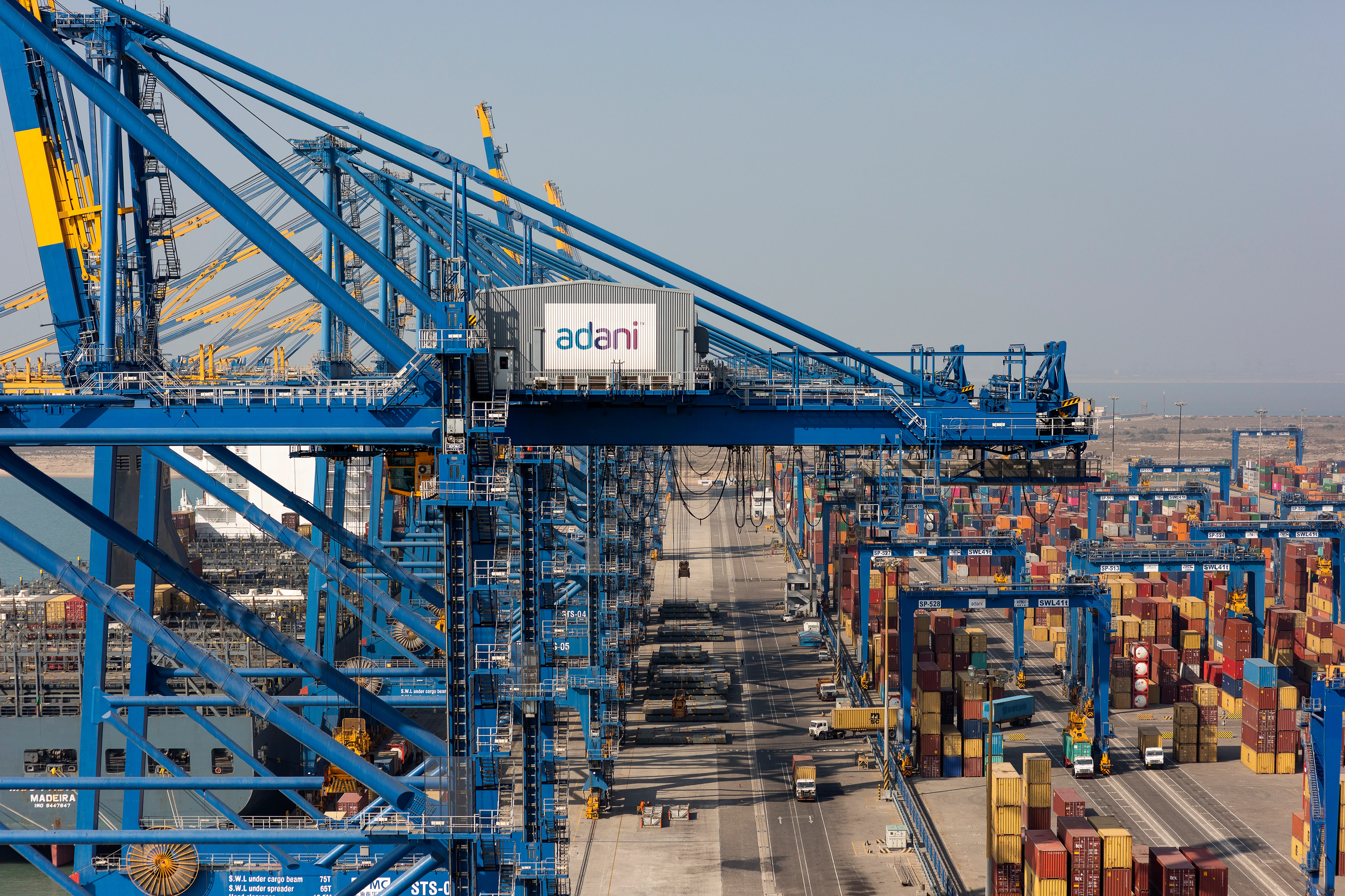 A large container ship being loaded or unloaded at a busy port terminal, with cranes and cargo visible.