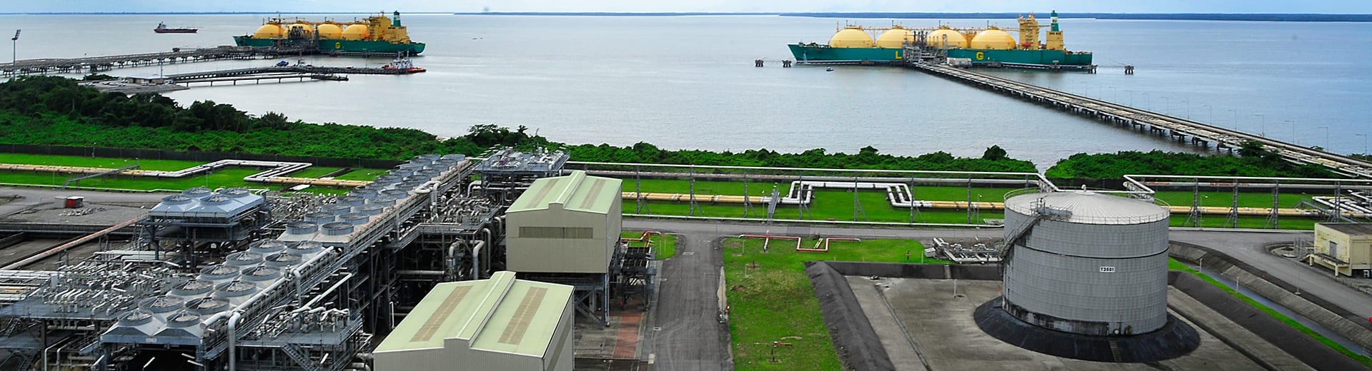 An LNG tanker at sea, with industrial facilities in the background.